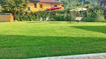 A well-maintained lawn with a patio area, a yellow building with a red roof, and a hill in the background.
