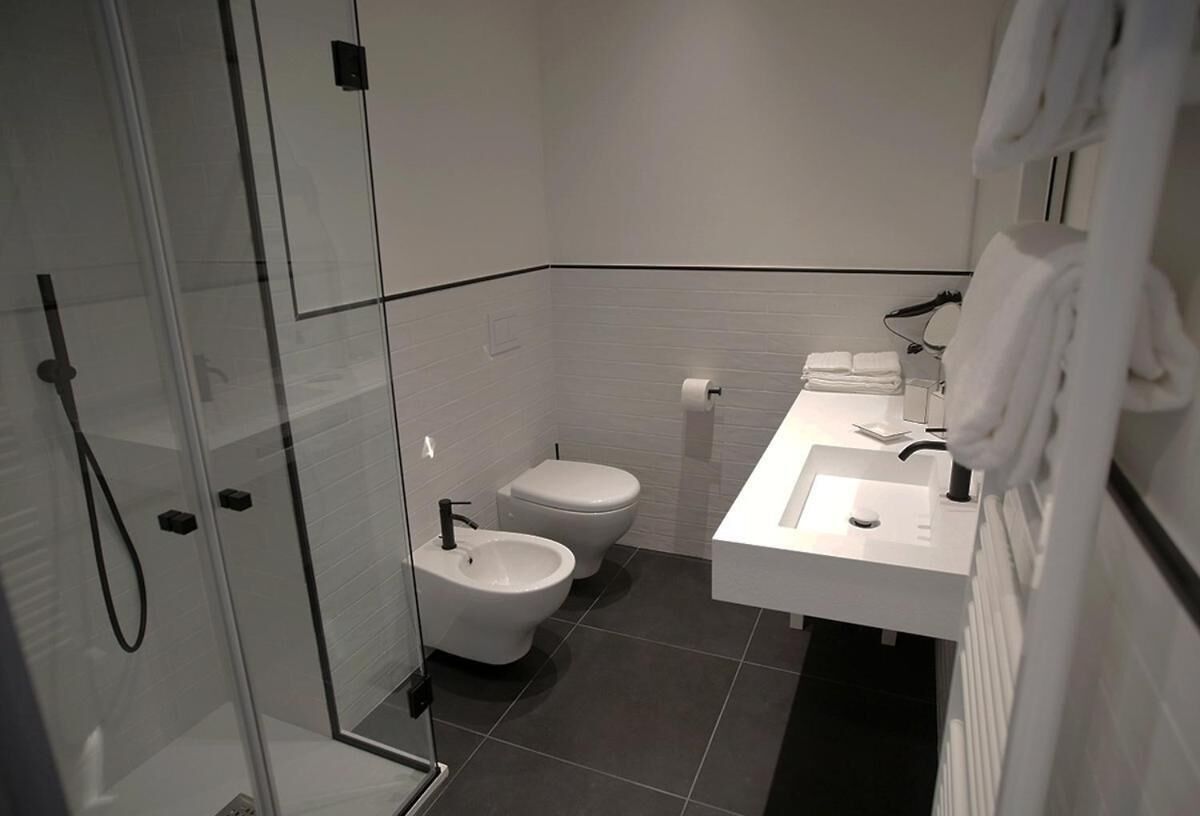 A modern bathroom with a glass shower enclosure, two toilets, a bidet, and a white sink with a mirror.