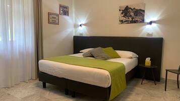 Una cama bien hecha con un plaid verde, una mesita de noche con un dispensador de pañuelos y dos lámparas fijadas a la pared.