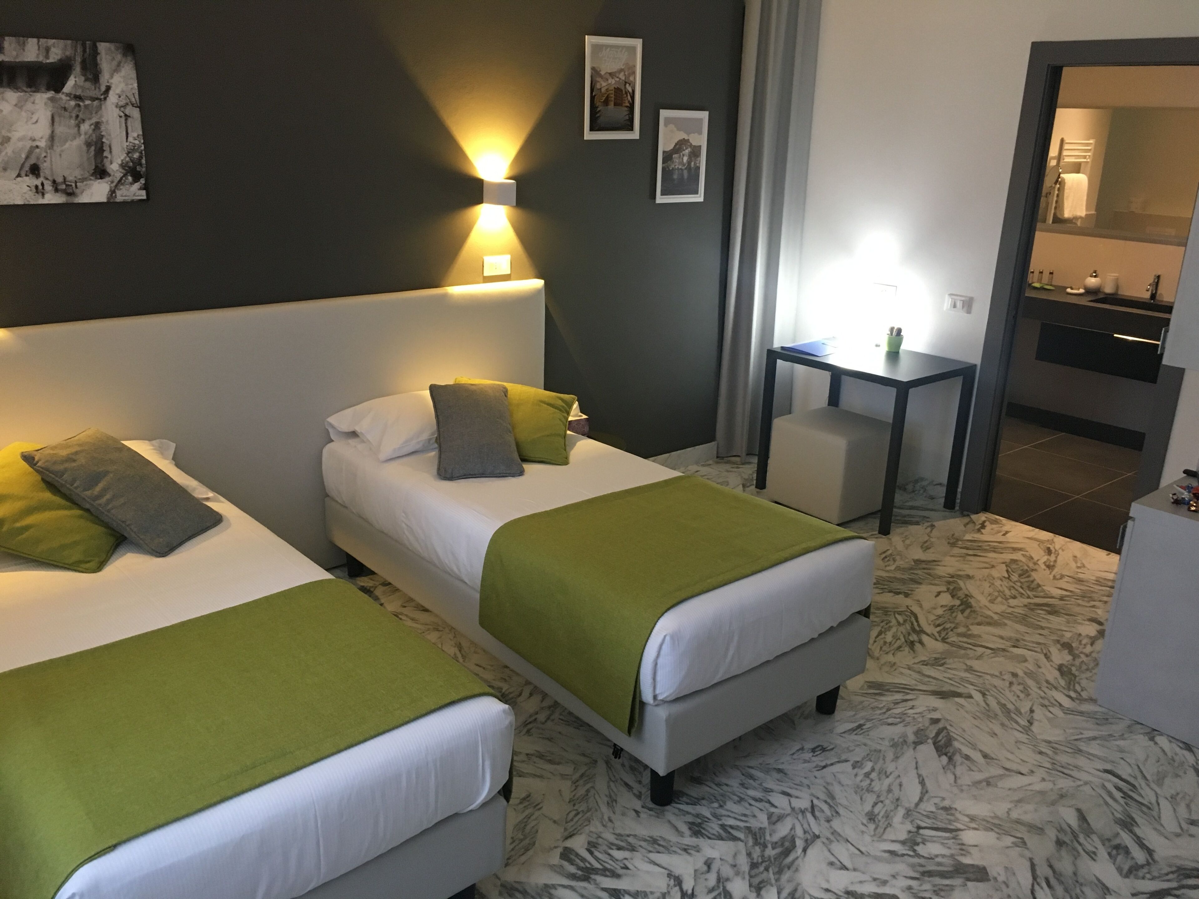Ein Hotelzimmer mit zwei Betten, einem kleinen Tisch, einem Sessel und einem durchgehenden Türspalt sichtbaren Bad.