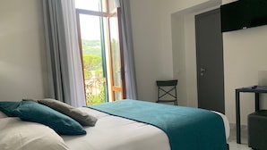 A neatly made bed with a teal blanket and pillows, a small table with a remote control, and a door to the right. - B&B Mikeme (Carrara)