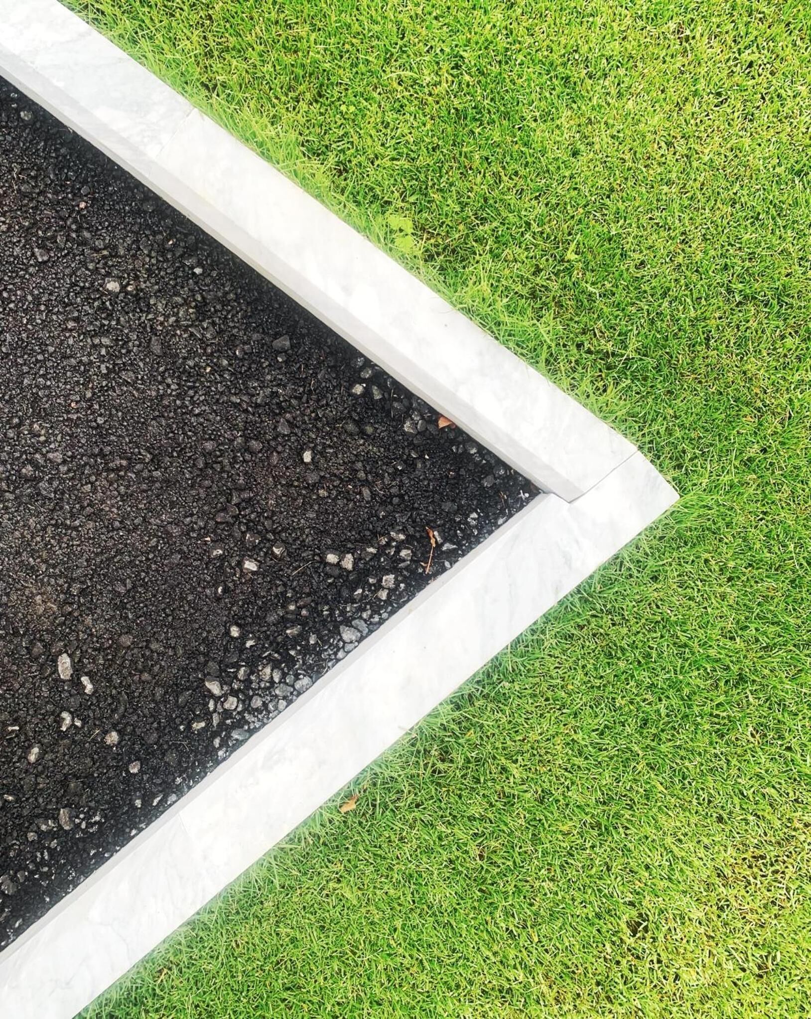 Un parterre de fleurs avec une terre sombre et une bordure blanche, entouré d’herbe verte.