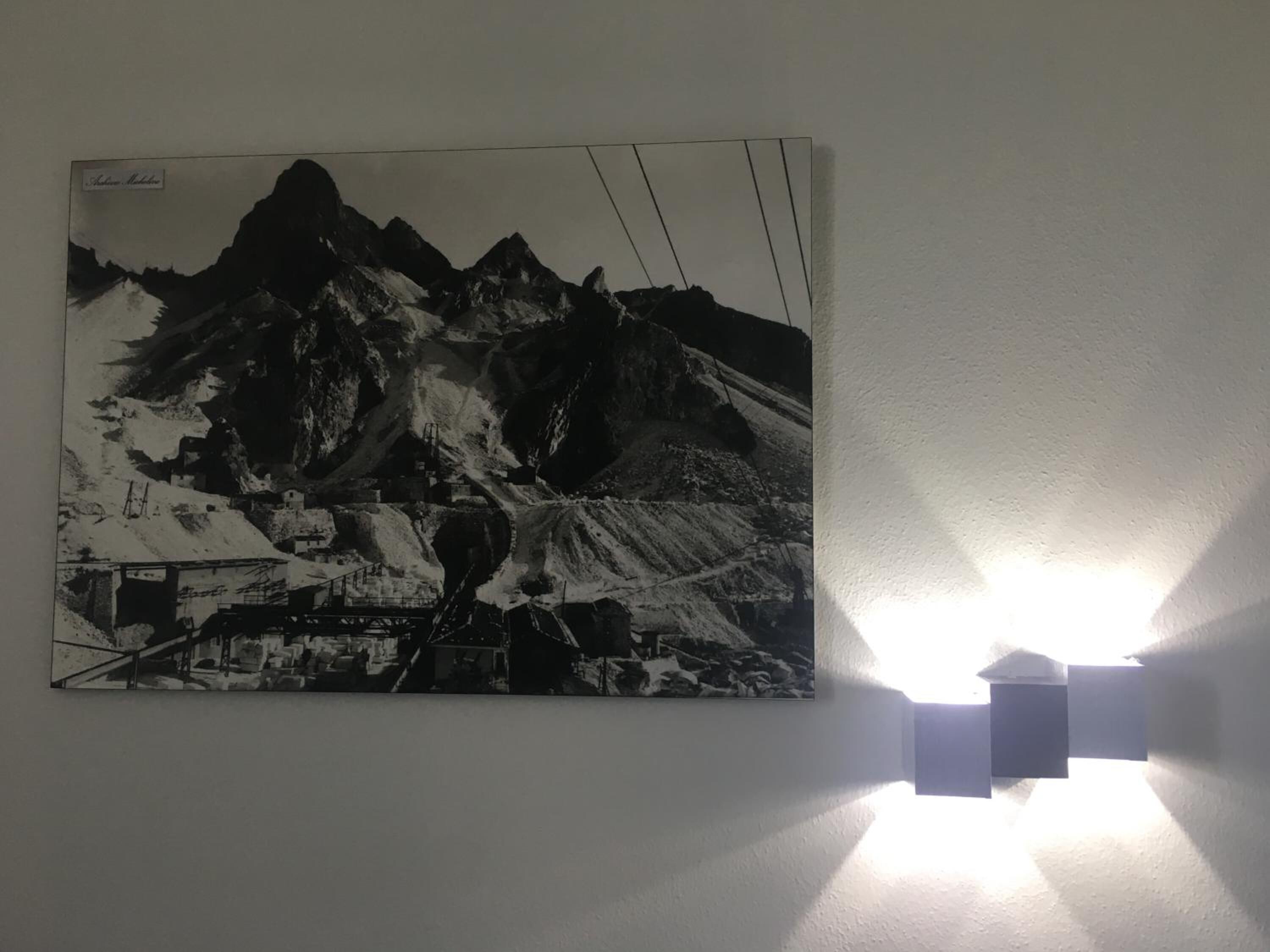 Fotografía en blanco y negro de un paisaje montañoso con una cabaña y un puente, expuesta en una pared.