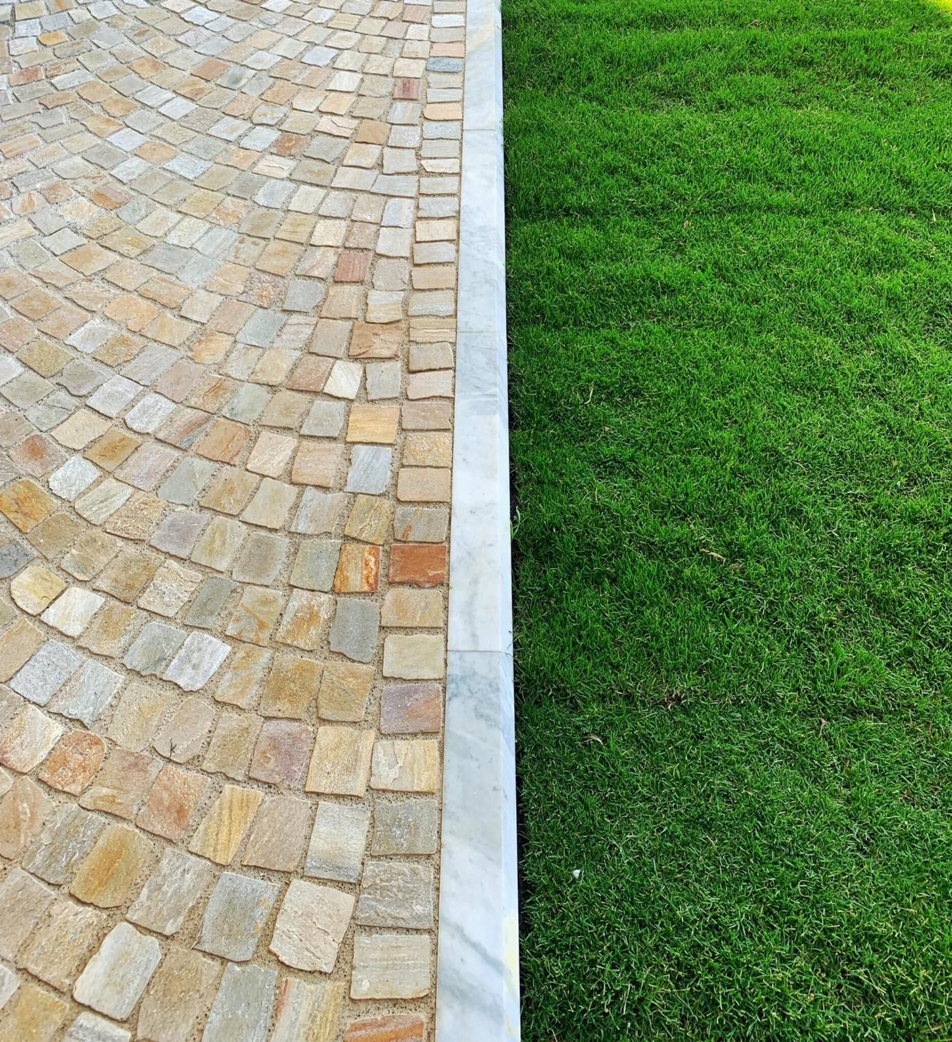 A stone pathway adjacent to a well-maintained lawn.