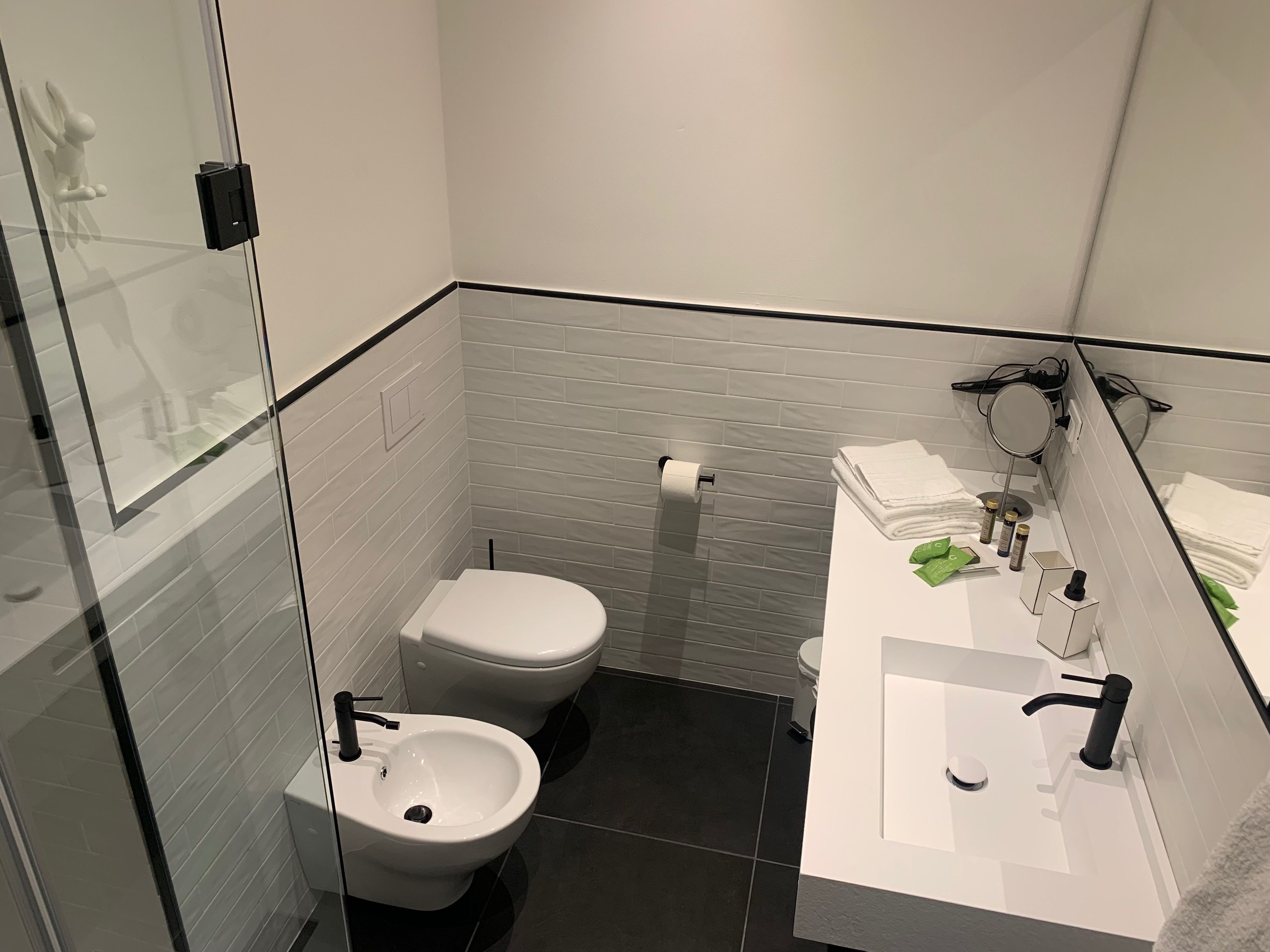 Un baño moderno con mampara de vidrio, inodoro, bidé, lavamanos con espejo y toallas ordenadas.