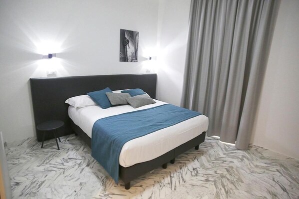 Un dormitorio con cama, dos lámparas de noche, una mesita redonda y un cuadro en la pared.
