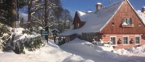 A snow-covered wooden cabin with a red roof, a sign indicating private parking, and a clear blue sky in the background.