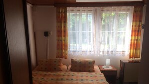 Ein Schlafzimmer mit einem Bett, zwei Kissen, einem Nachttisch mit Lampe und einem Fenster mit Vorhängen.