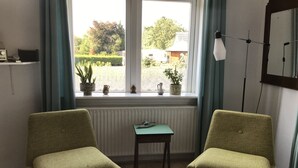 Ein Zimmer mit zwei grünen Sesseln, einem kleinen Tisch und einem Fenster mit Vorhängen.