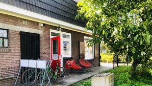 Ein Backsteinhaus mit roter Tür, einem weißen Tisch und zwei roten Stühlen davor.