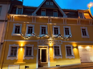 Un bâtiment jaune avec une enseigne indiquant « BRANFELS ». Il possède de nombreuses fenêtres et une porte, et la façade est illuminée.