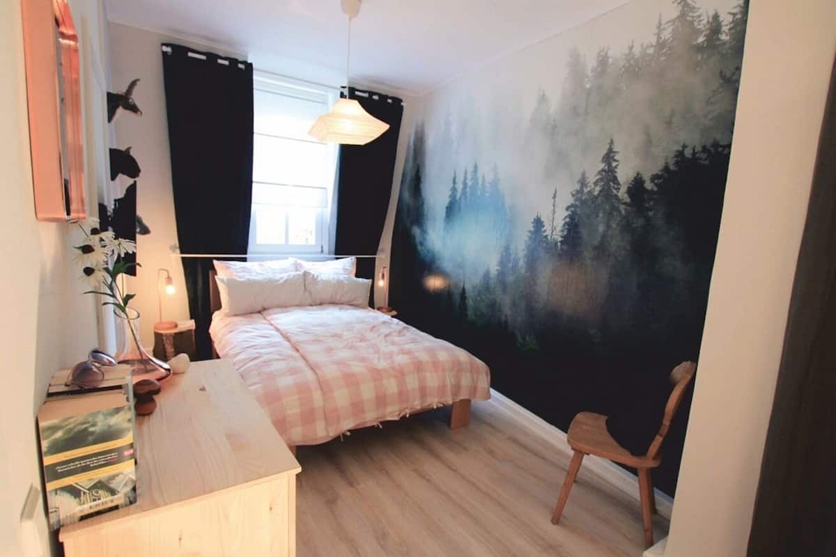Une chambre à coucher comprenant un lit, une chaise, un bureau, une fenêtre et une fresque représentant une forêt sur le mur.