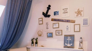 Una stanza con una sedia di legno, un termosifone bianco e decorazioni a tema nautico, tra cui ancore e una stella marina.