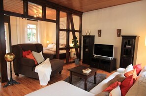 Un salon meublé avec un canapé, un fauteuil, une table basse, un téléviseur et un lit à l’arrière-plan.