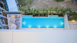 A rectangular swimming pool with a tiled edge, surrounded by a low wall and a row of umbrellas.