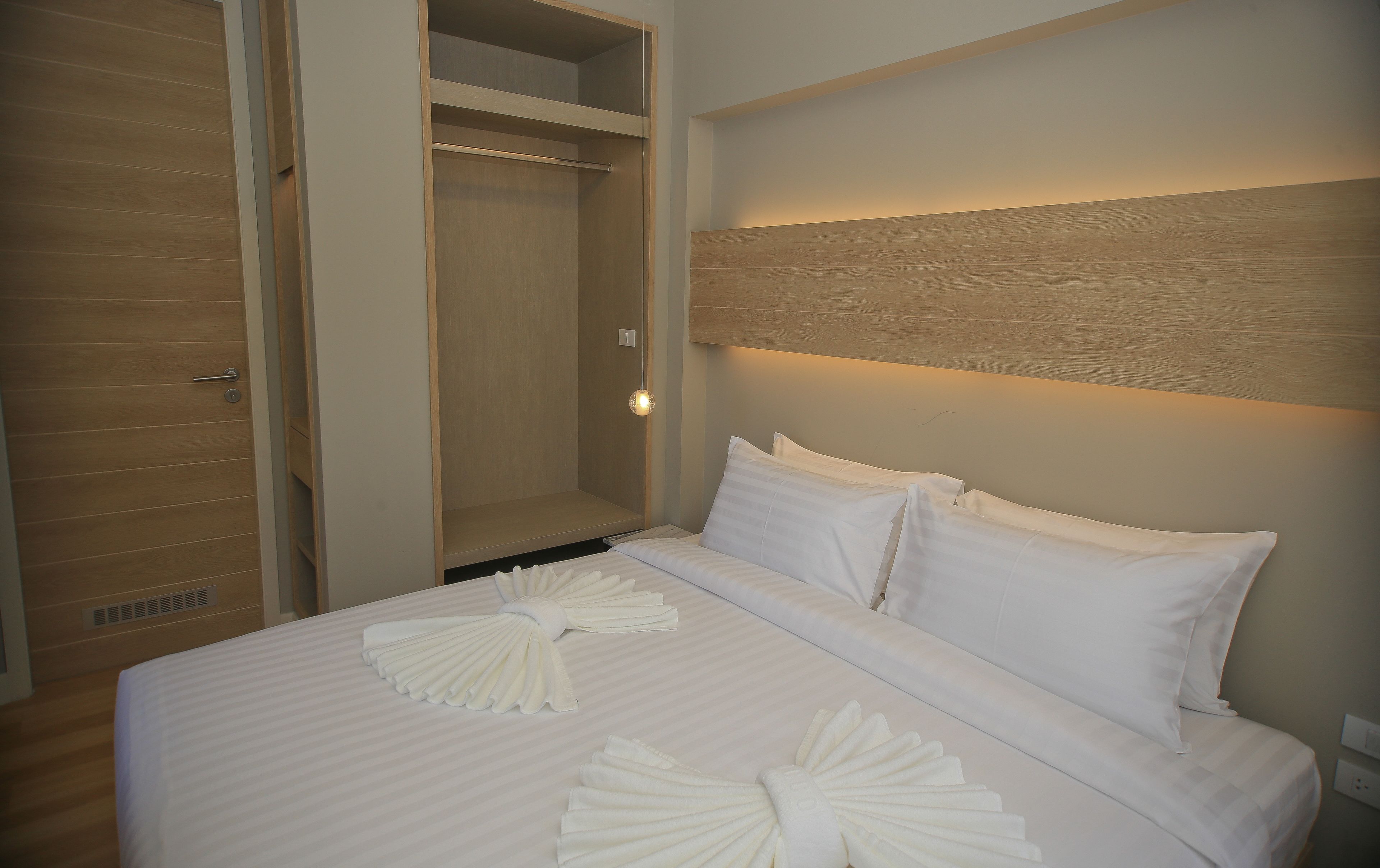 Een hotelkamer met een bed, witte lakens, een houten hoofdeinde en een inloopkast.