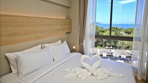 A hotel room with a large bed, a wooden headboard, and a view of the ocean through sheer curtains.