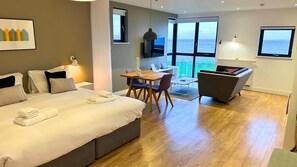 Una habitación de hotel moderna con una cama, una mesa de comedor, un sofá y vista al mar.