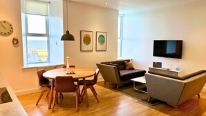 A modern living room with a round wooden table, a sofa, a TV, and artwork on the wall.