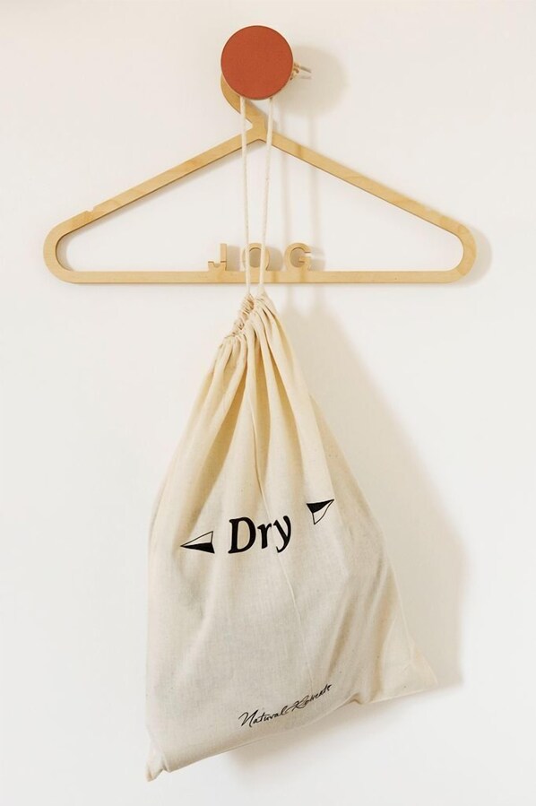 Una borsa beige con coulisse appesa a un appendiabiti di legno, con la scritta 'Dry' e un simbolo.