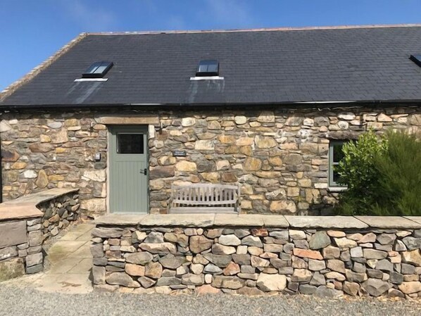 Une maison en pierre avec une porte verte, un petit banc et une fenêtre.