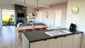 Een moderne keuken met een centraal eiland, een eethoek met een houten tafel en een woonruimte met een bank en een televisie.