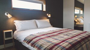 Een slaapkamer met een bed, twee bedlampen, een raam en een spiegel.