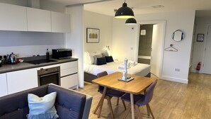 A modern, compact hotel room with a kitchenette, a dining area, a bed with a bathroom visible through an open door, and a hallway with a mirror and a fire extinguisher. - A john o'groat that sleeps 2 guests  in 1 bedroom (Wick)