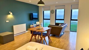 A modern living room with a wooden table, two chairs, a sofa, and a TV mounted on the wall. - A john o'groat that sleeps 2 guests  in 1 bedroom (Wick)