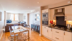 A modern kitchen with a stove, oven, and microwave. There is a dining area with a table and chairs. - A fistral beach that sleeps 4 guests  in 2 bedrooms (Newquay)