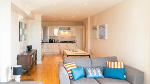 A modern living room with a grey sofa, a wooden coffee table, and a dining area with a table and chairs. - A fistral beach that sleeps 4 guests  in 2 bedrooms (Newquay)