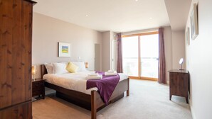 A bedroom with a bed, wooden wardrobe, bedside table, and a large window with curtains. - A fistral beach that sleeps 4 guests  in 2 bedrooms (Newquay)