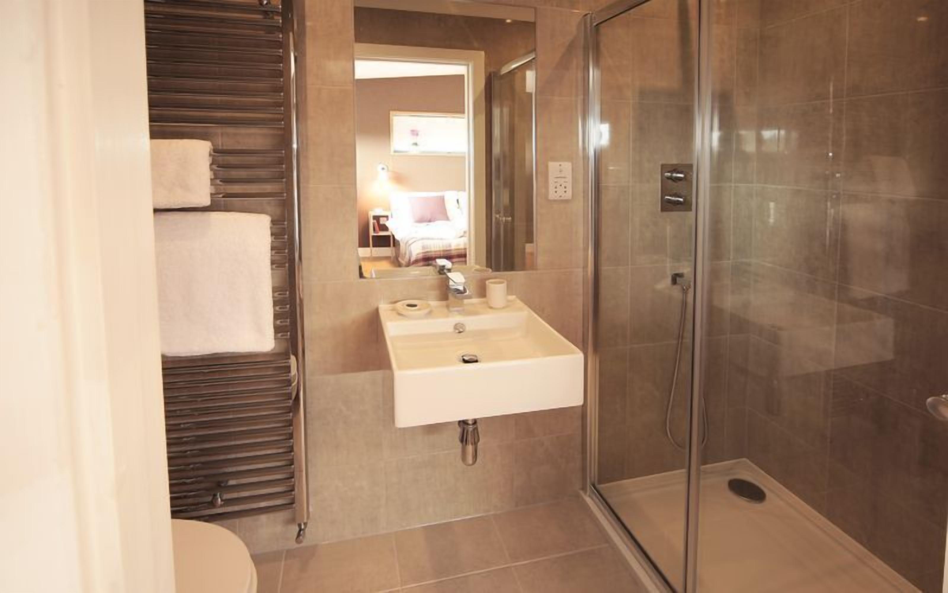 A bathroom with a glass shower enclosure, a sink with a mirror, and a towel rack.