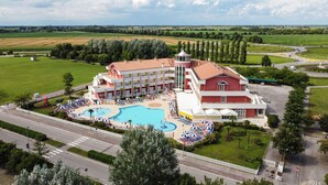 A hotel with a swimming pool, multiple balconies, and a view of surrounding fields. - Hotel Olympus (Caorle)