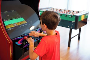 Ett barn spelar ett videospel på en spelkonsol, och i bakgrunden syns ett bordfotbollsspel.