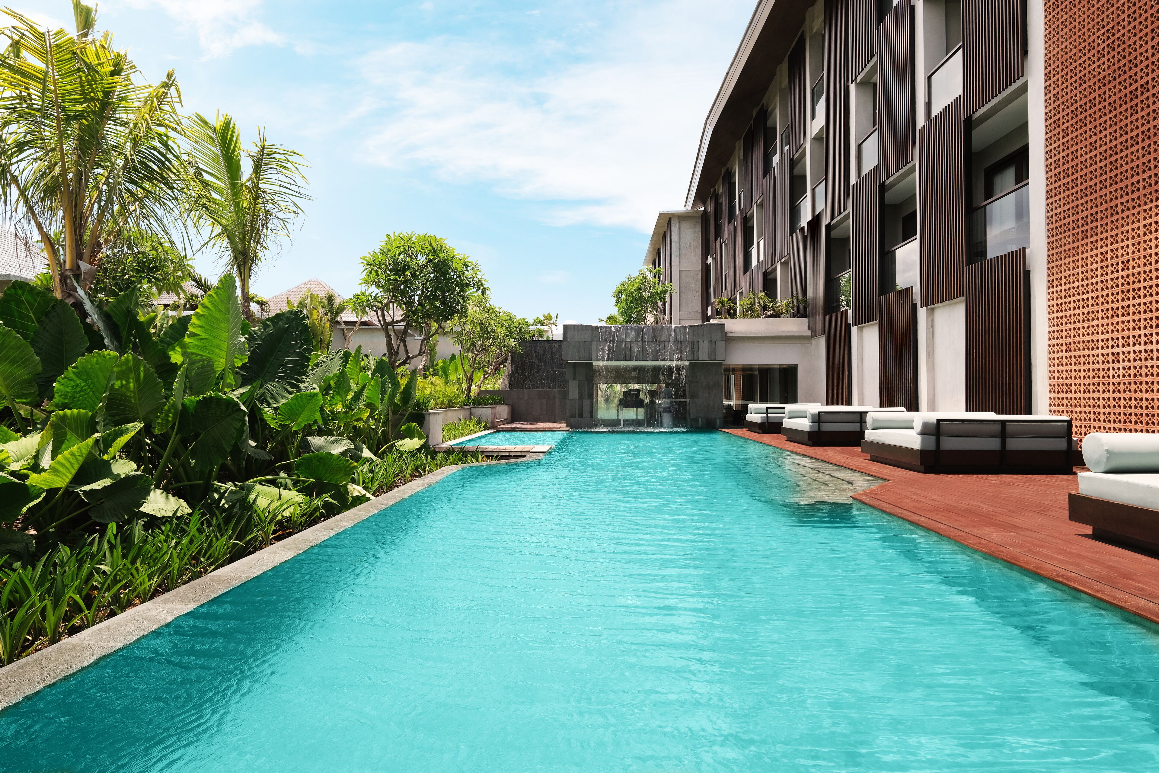 A modern hotel pool area with a clear pool, lounge chairs, and lush greenery.