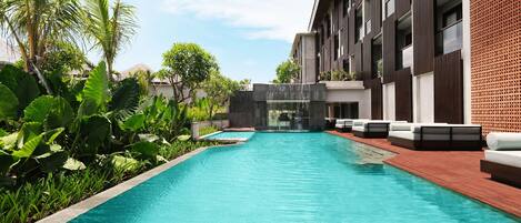 Zona de piscina moderna de hotel con piscina cristalina, sillas de descanso y abundante vegetación.