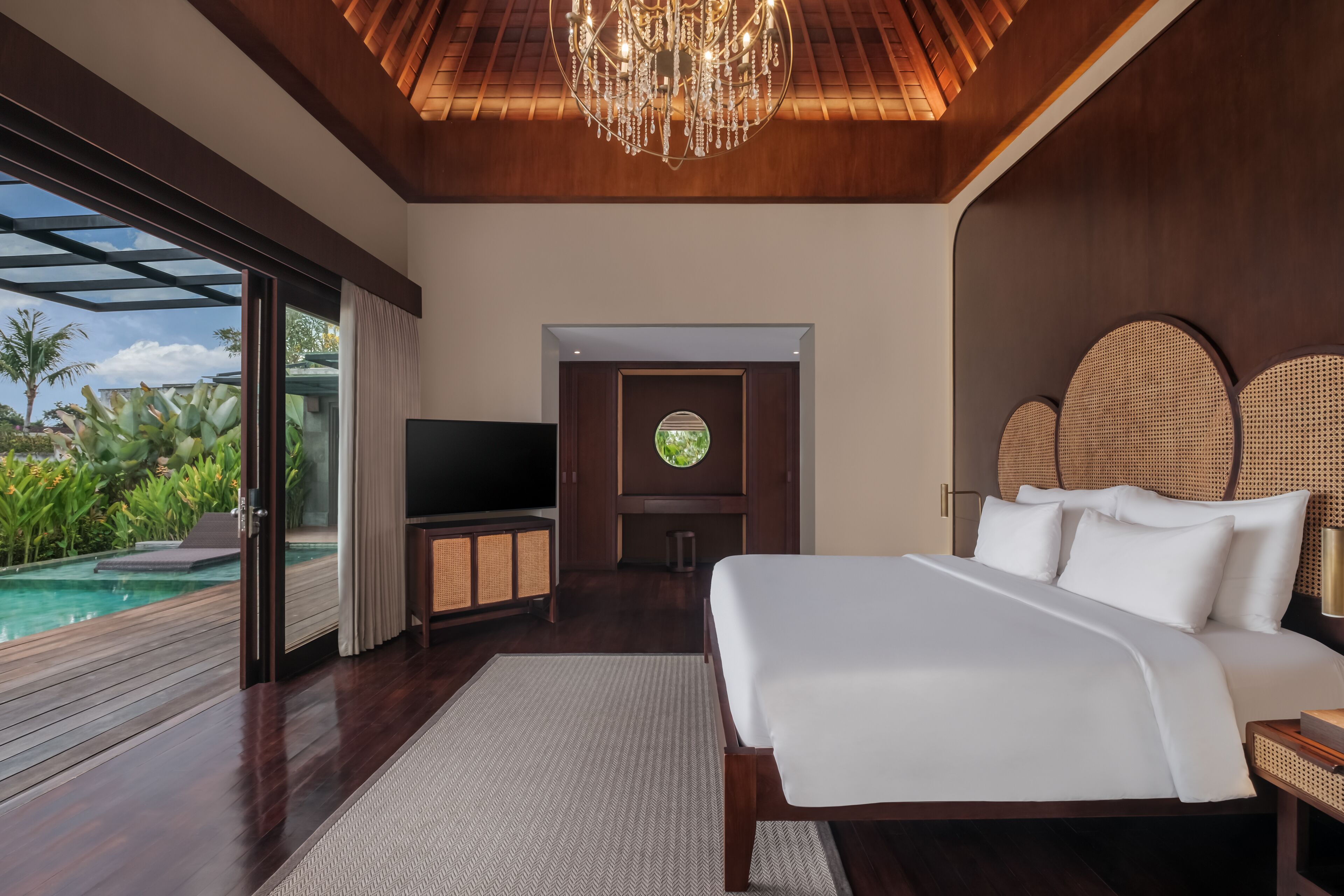 A bedroom with a large bed, a TV, and a view of a pool.