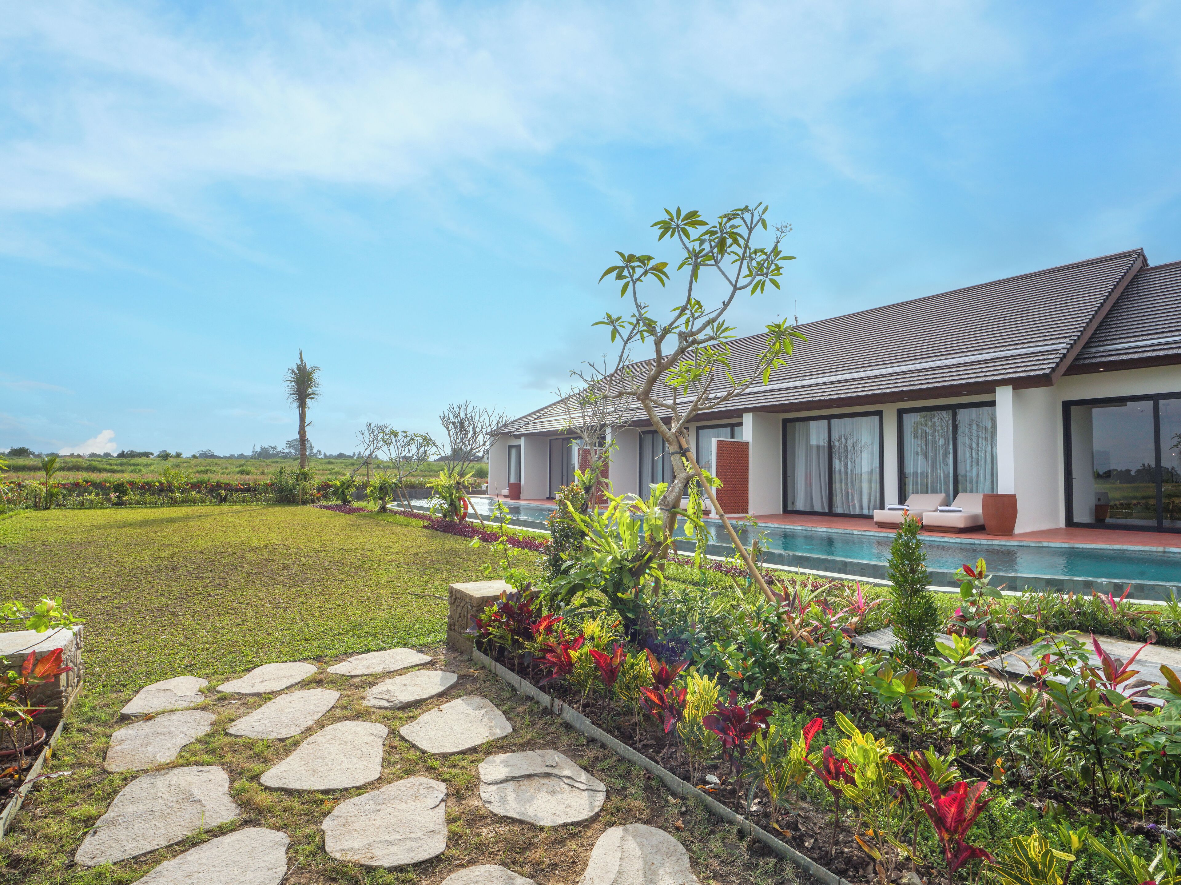 Uma casa moderna com piscina, rodeada por um jardim bem cuidado e um caminho de pedra.