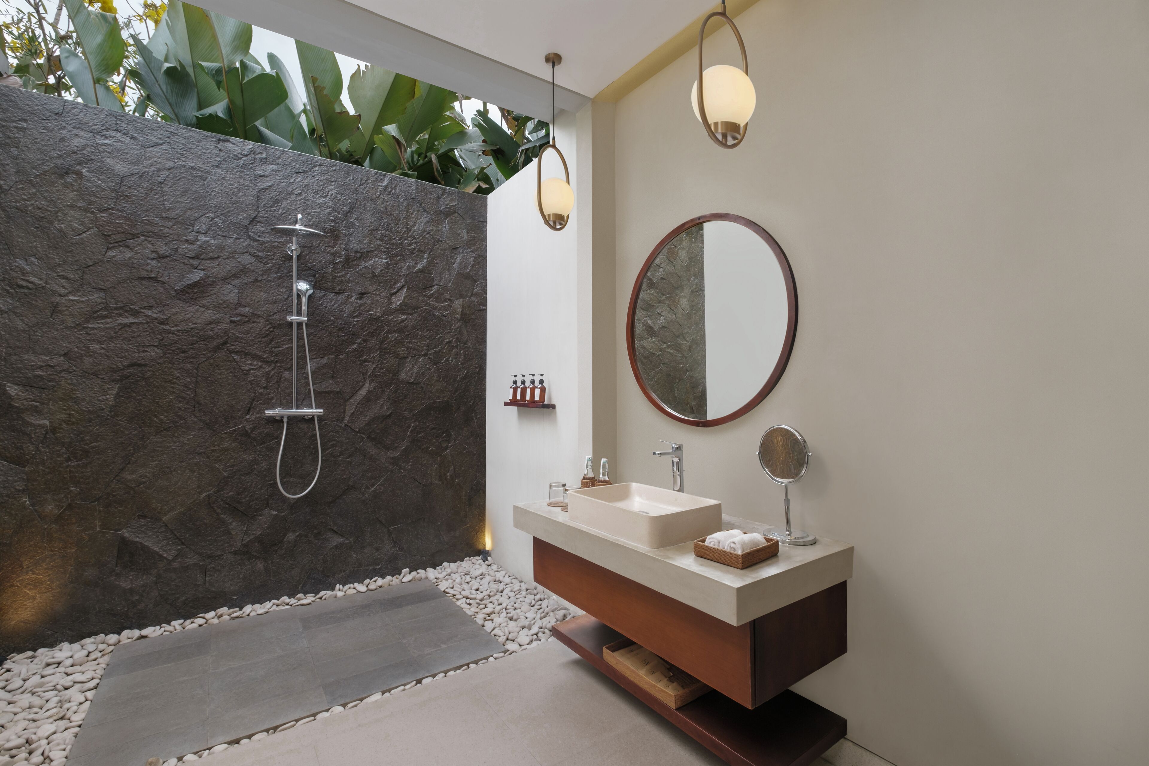 Een moderne badkamer met een stenen muur, een losstaande douche, een wastafel met spiegel en een kleine plant.