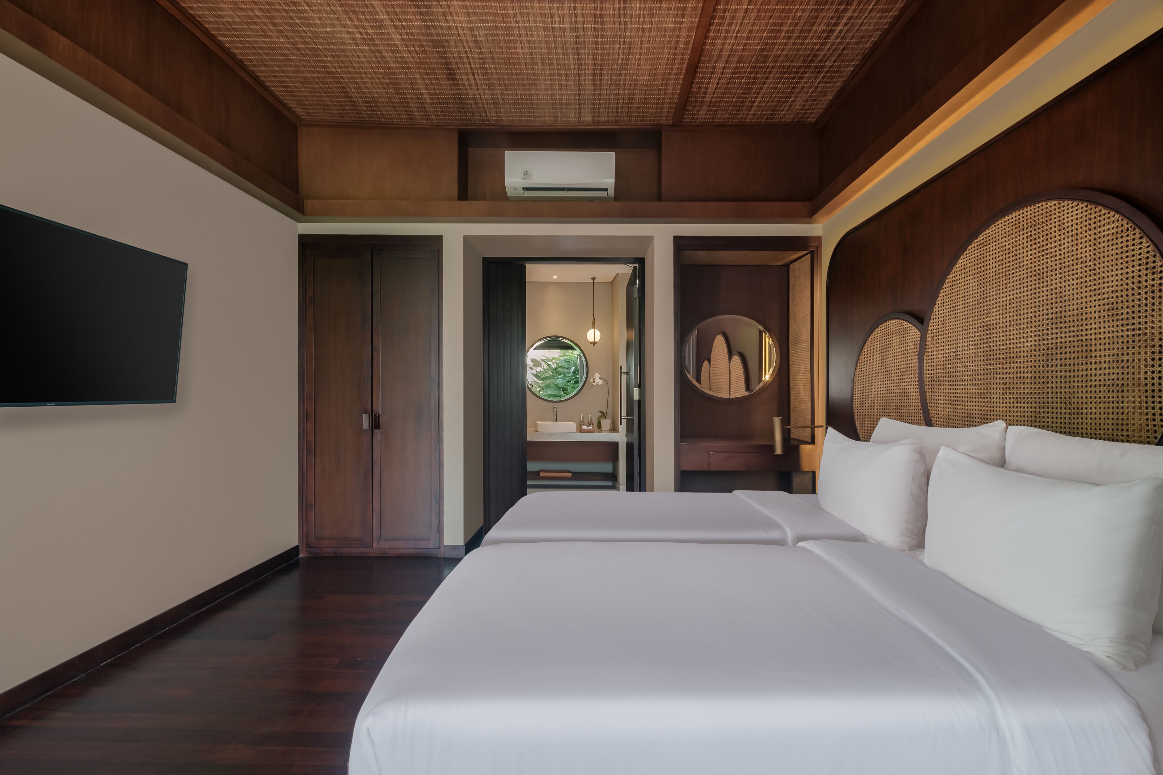 A hotel room with a large bed, a flat-screen TV mounted on the wall, a wooden ceiling, and a bathroom visible through an open door.