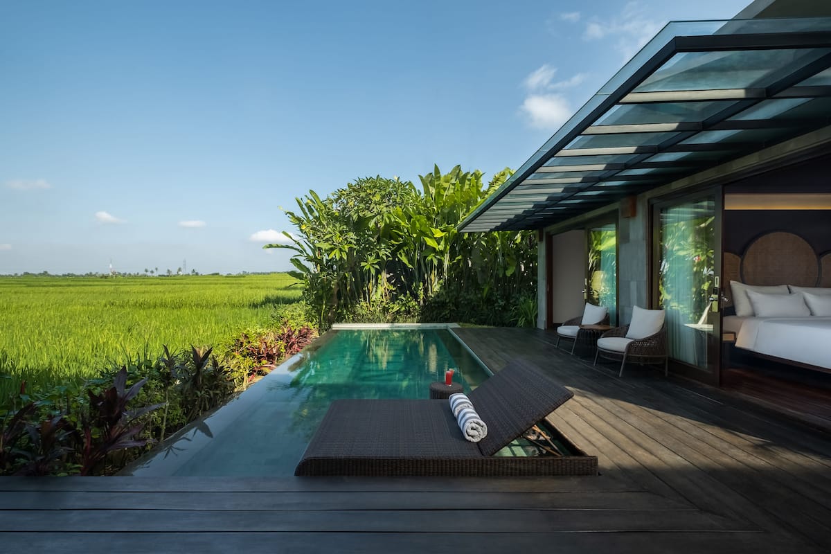 A modern outdoor pool area with a glass ceiling, surrounded by lush greenery and a view of a green field.