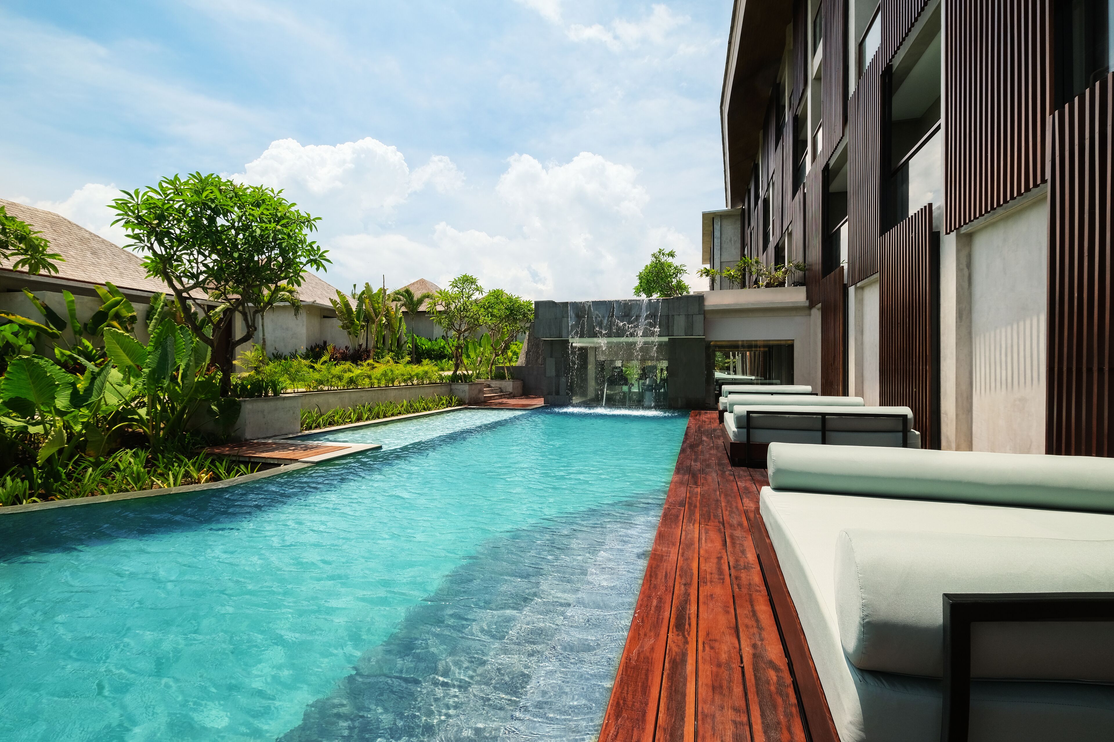 A swimming pool with a wooden deck, a waterfall feature, and outdoor seating.
