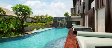 A swimming pool with a wooden deck, a waterfall feature, and outdoor seating.
