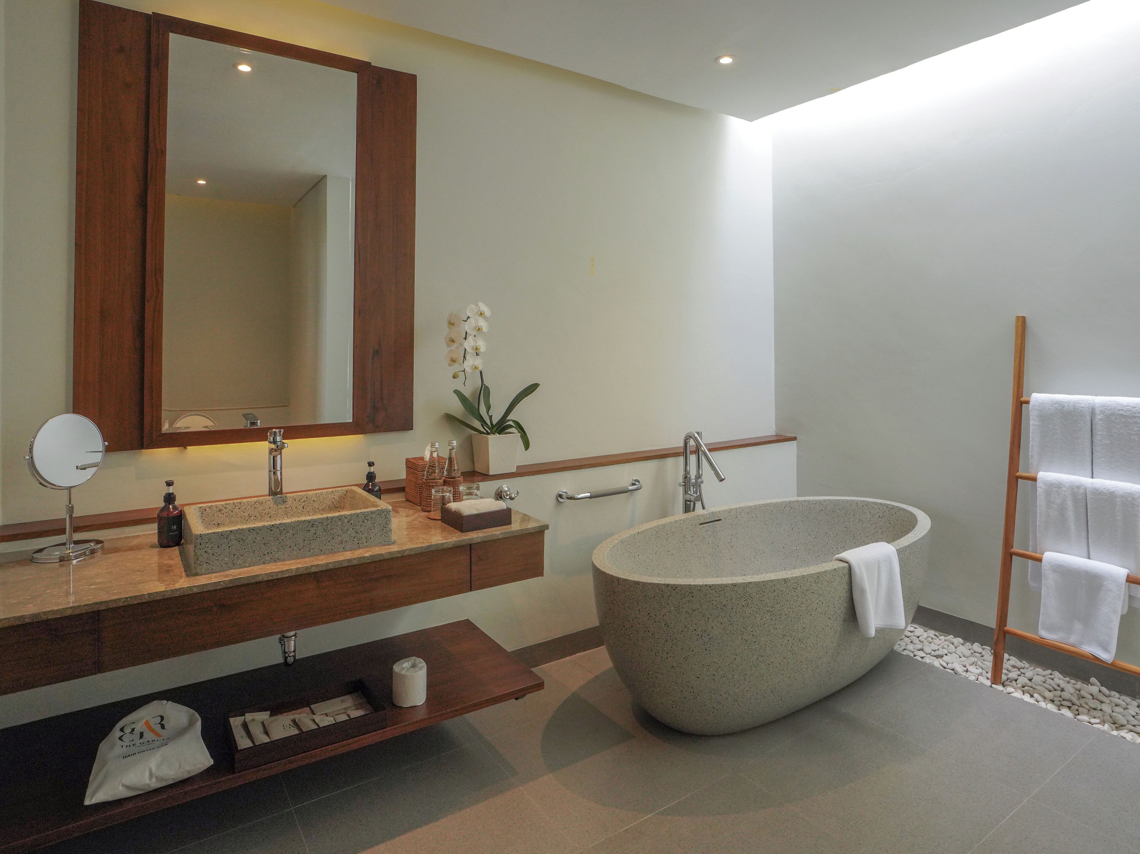 Un baño moderno con una bañera independiente, un espejo grande, un tocador de madera y un perchero para toallas.