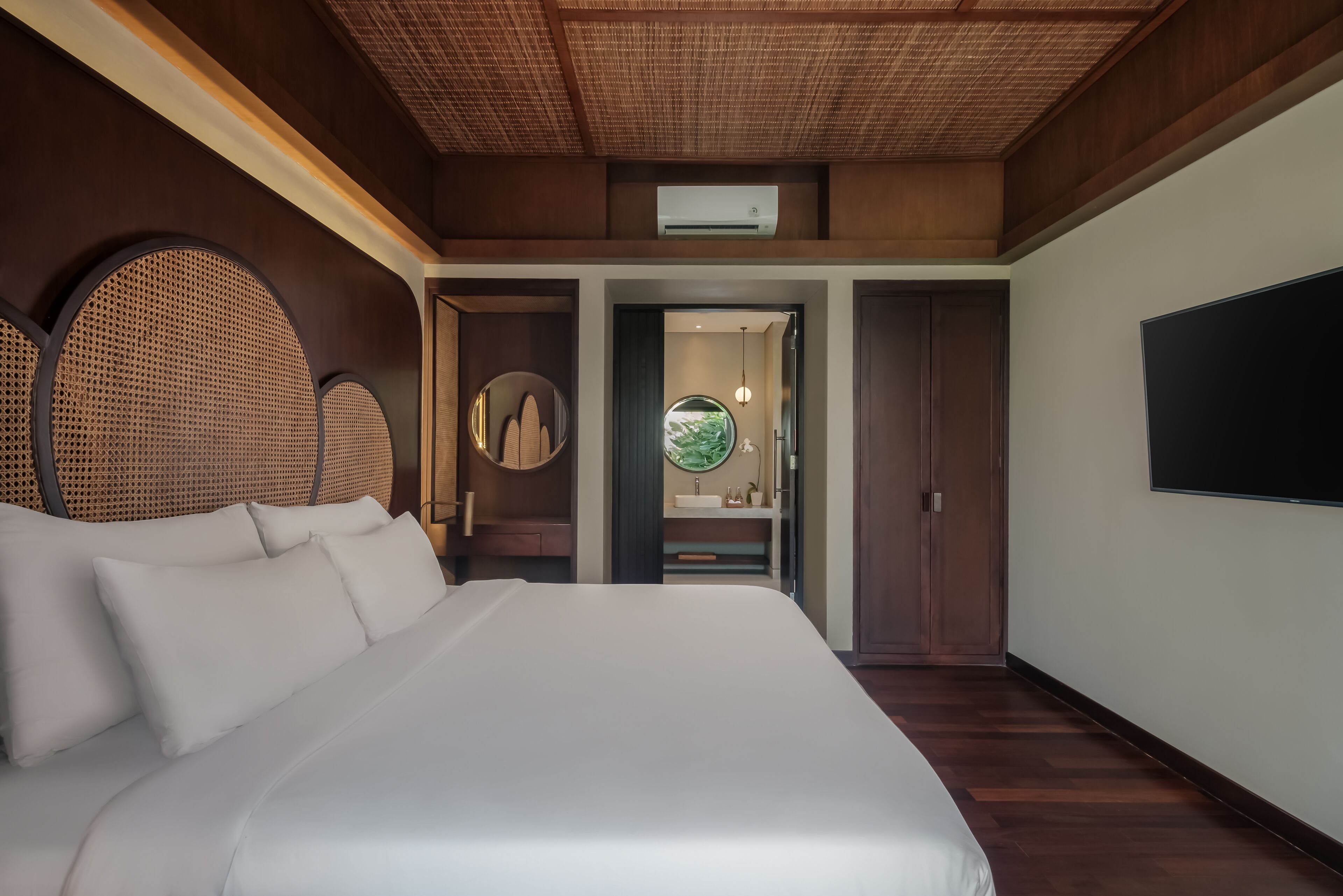Un dormitorio con una cama grande, televisor, baño con lavamanos y espejo, y ventilador de techo.