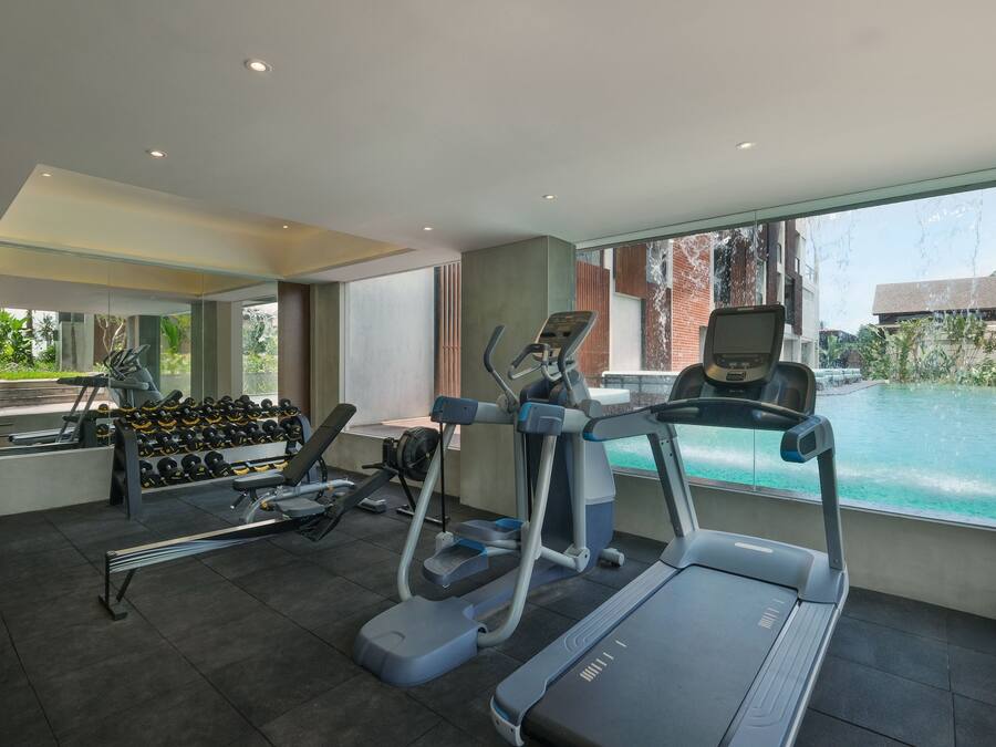 A gym with treadmills, ellipticals, and dumbbells, overlooking a swimming pool.