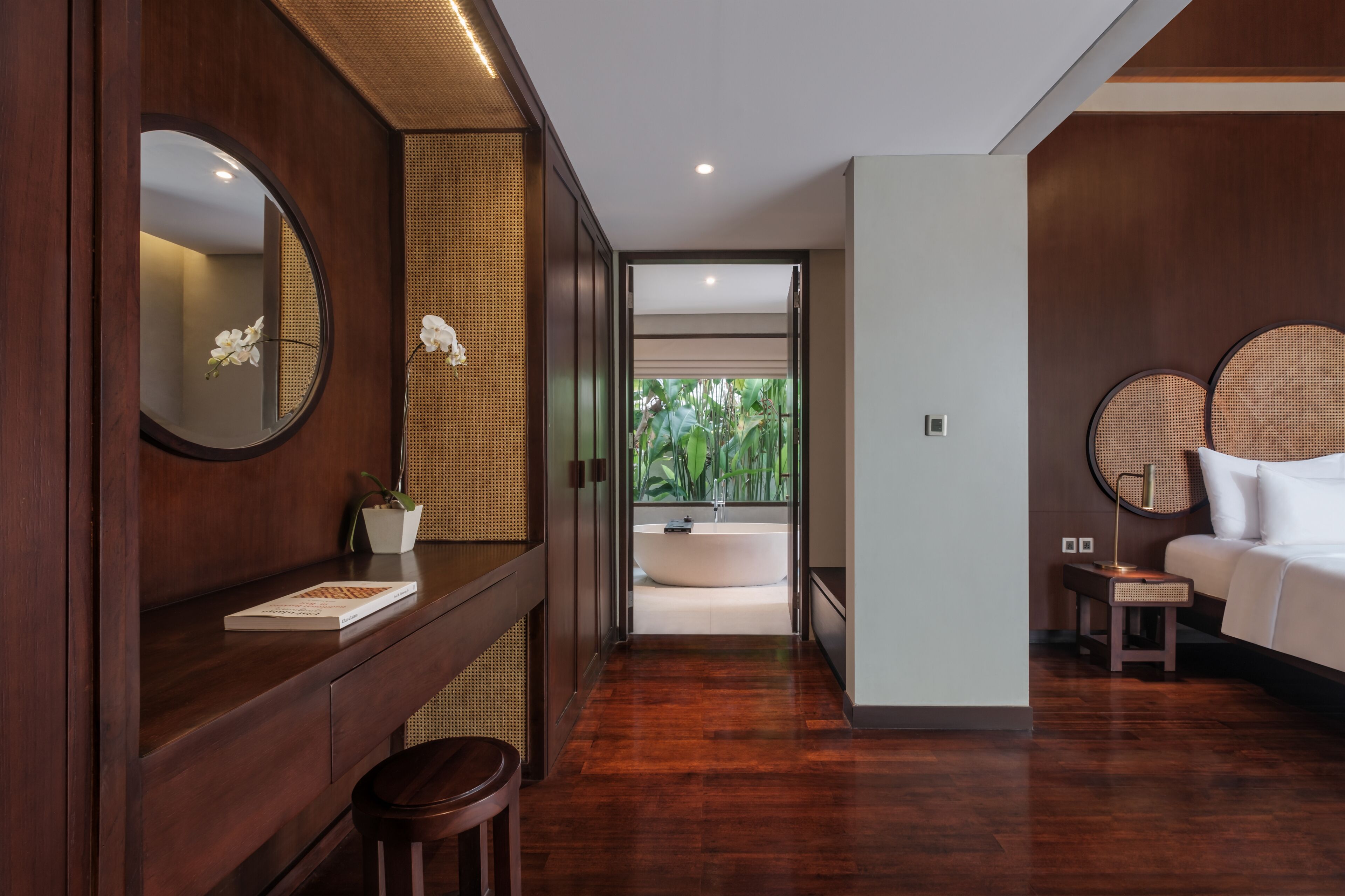 A modern bathroom with a freestanding bathtub, a wooden vanity with a mirror, and a bedside table with a lamp.