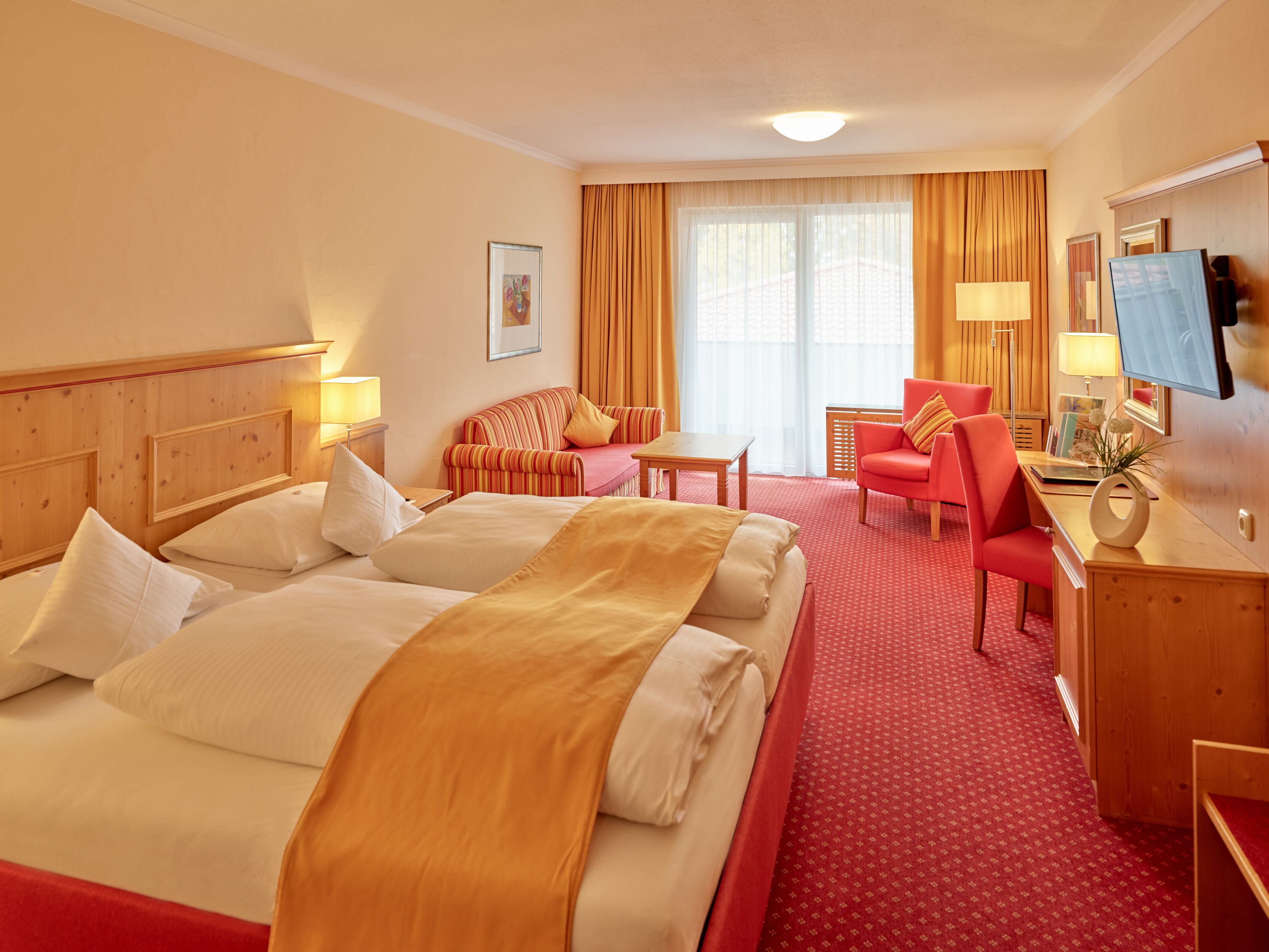 A hotel room with two beds, a desk, a chair, a TV, and a window with curtains.