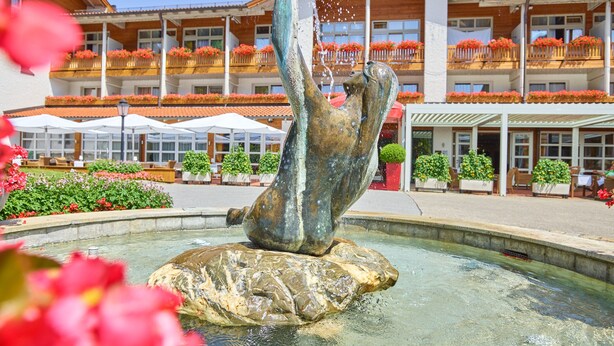 A fountain sculpture in a courtyard with a building featuring balconies with flower boxes in the background. - Parkhotel Bad Griesbach (Bad Griesbach im Rottal)